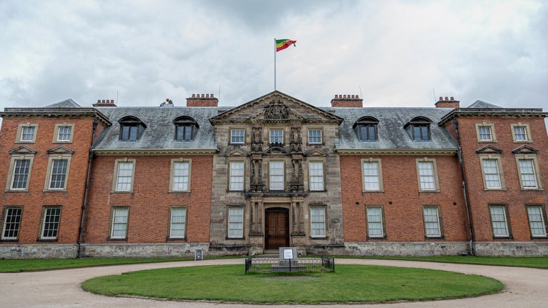 Lion of Judah flag raised above the house at Dunham Massey with a grass circle in the foreground and white clouds in the background
